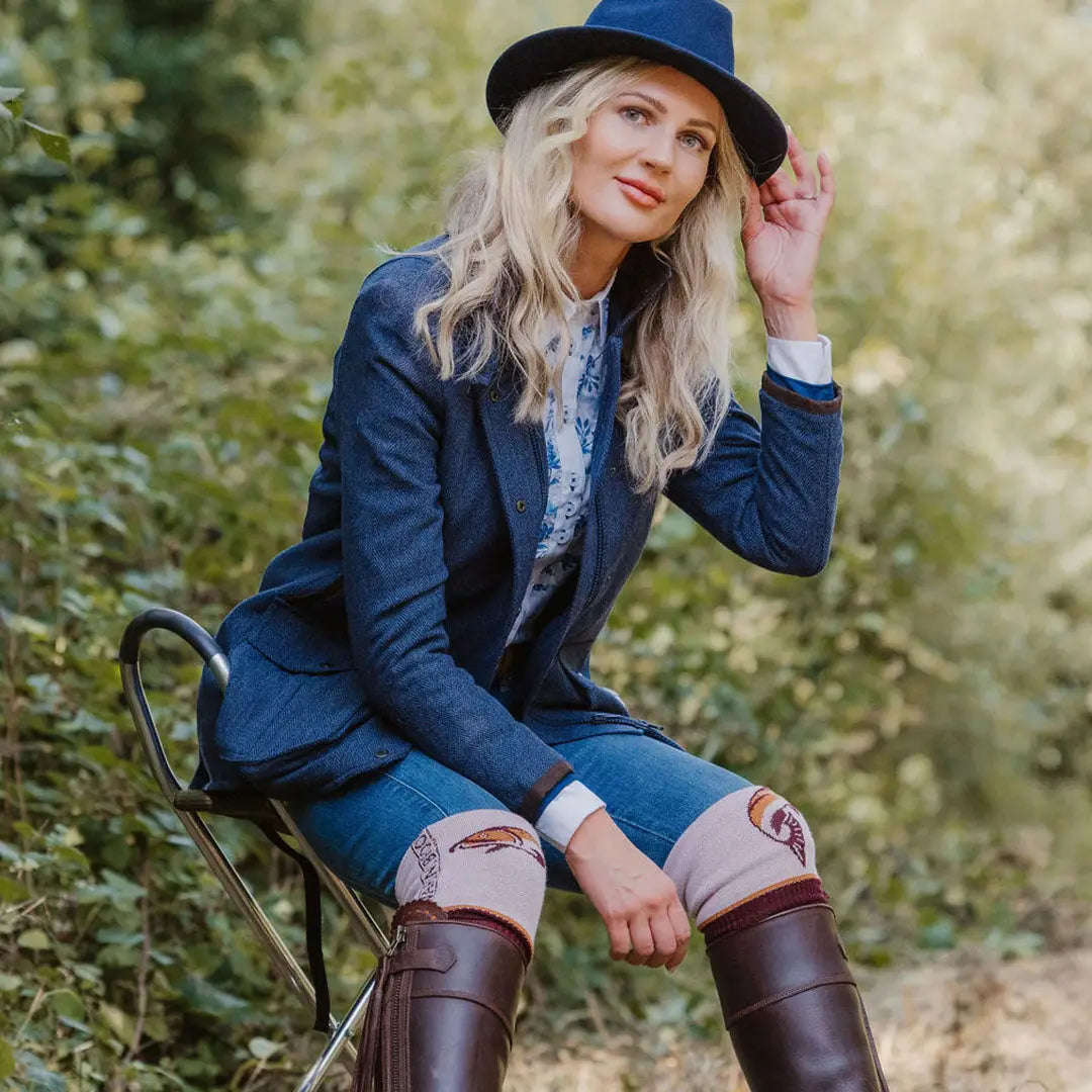 Woman in blue hat and forest Jessica Tweed Field Coat sitting outdoors on a chair