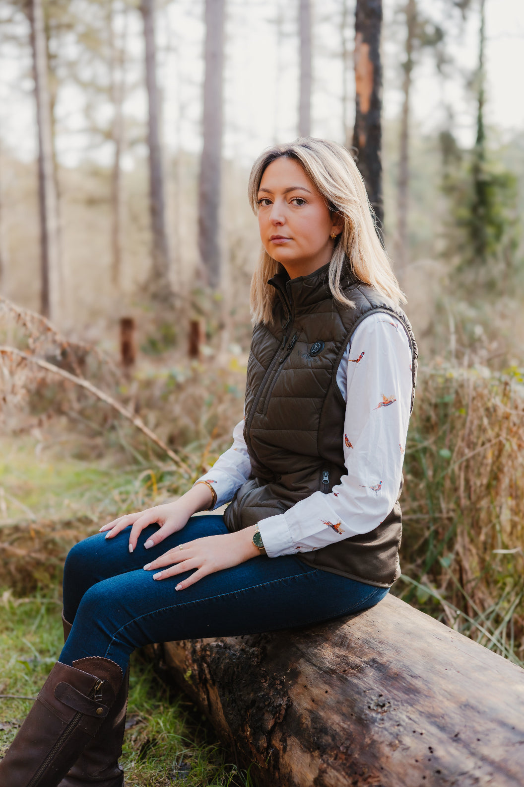 Woman in a vest relaxing on a log wearing a New Forest Ladies Heated Gilet