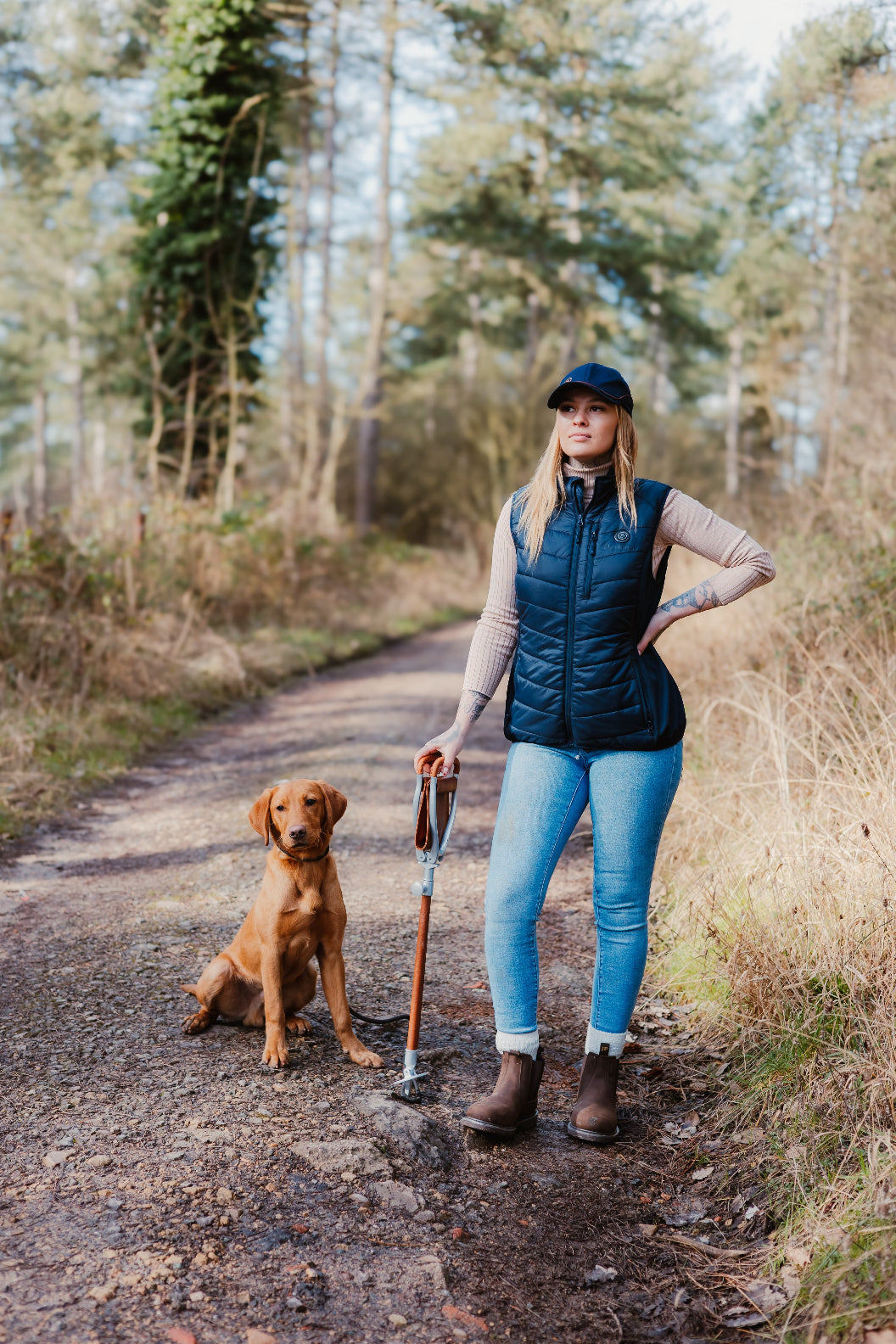 Woman with dog enjoying a walk in the woods wearing a stylish Forest Heated Gilet