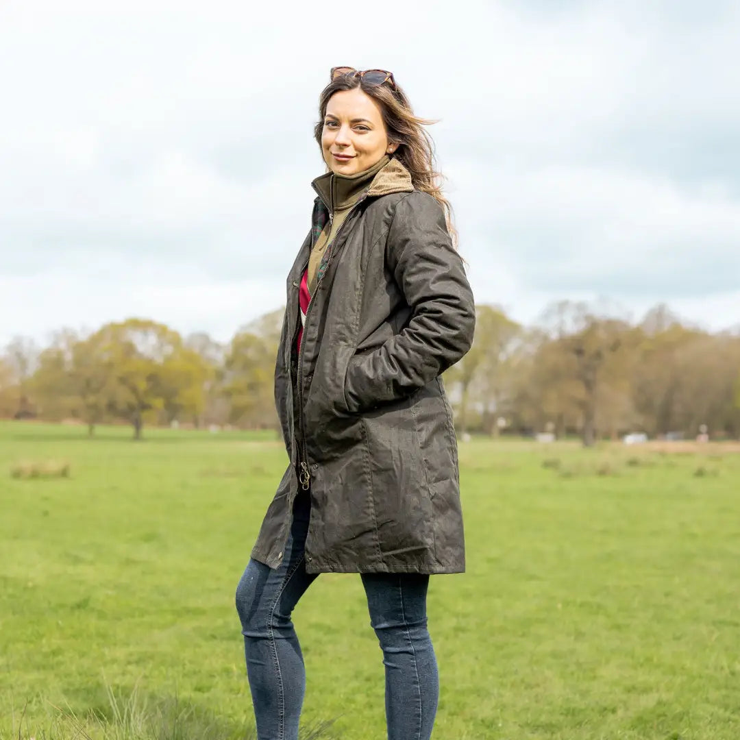 Woman in dark coat in grassy field, showcasing New Forest Ladies Longer Length Wax Jacket