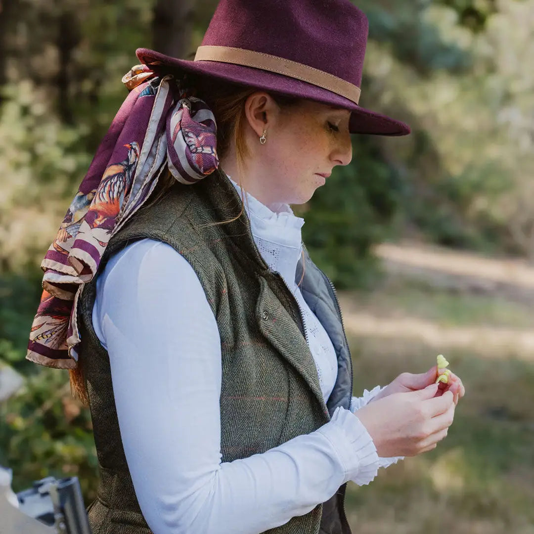 Woman in a purple hat checks out her hands while wearing a New Forest Ladies Tweed Gilet