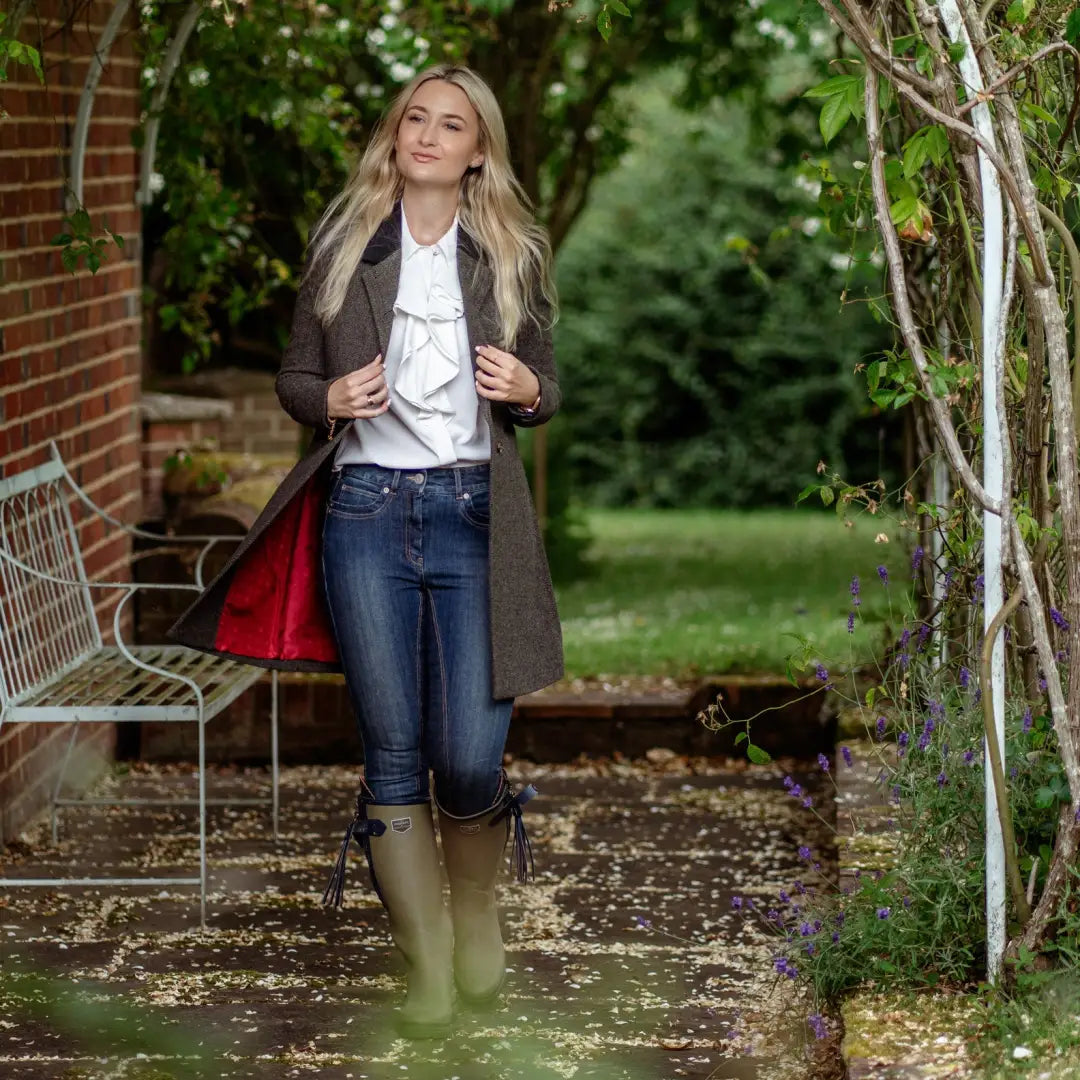 Woman in a garden wearing a Forest Lizzie Tweed Coat, jeans, and rain boots