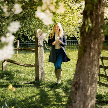 Woman by a wooden fence in the forest wearing the stylish Lizzie Tweed Coat