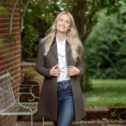 Smiling blonde woman in a Forest Lizzie Tweed coat over white top and jeans