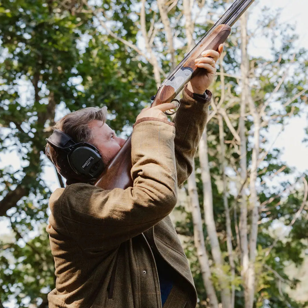 Person aiming a shotgun while wearing a New Forest Maverick Waterproof Tweed Jacket