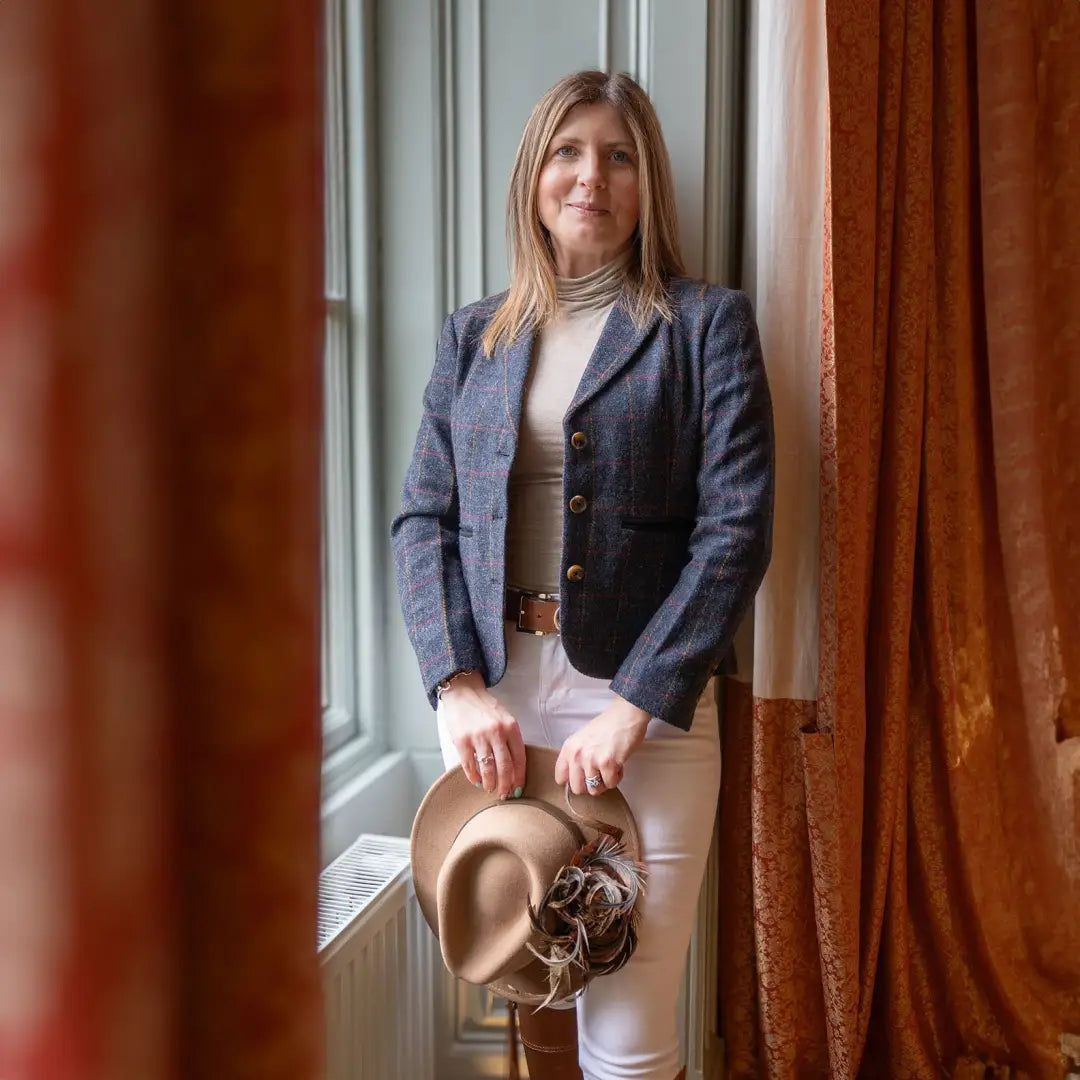 Woman in a navy Forest Polly Tweed Blazer and white pants holding a tan hat