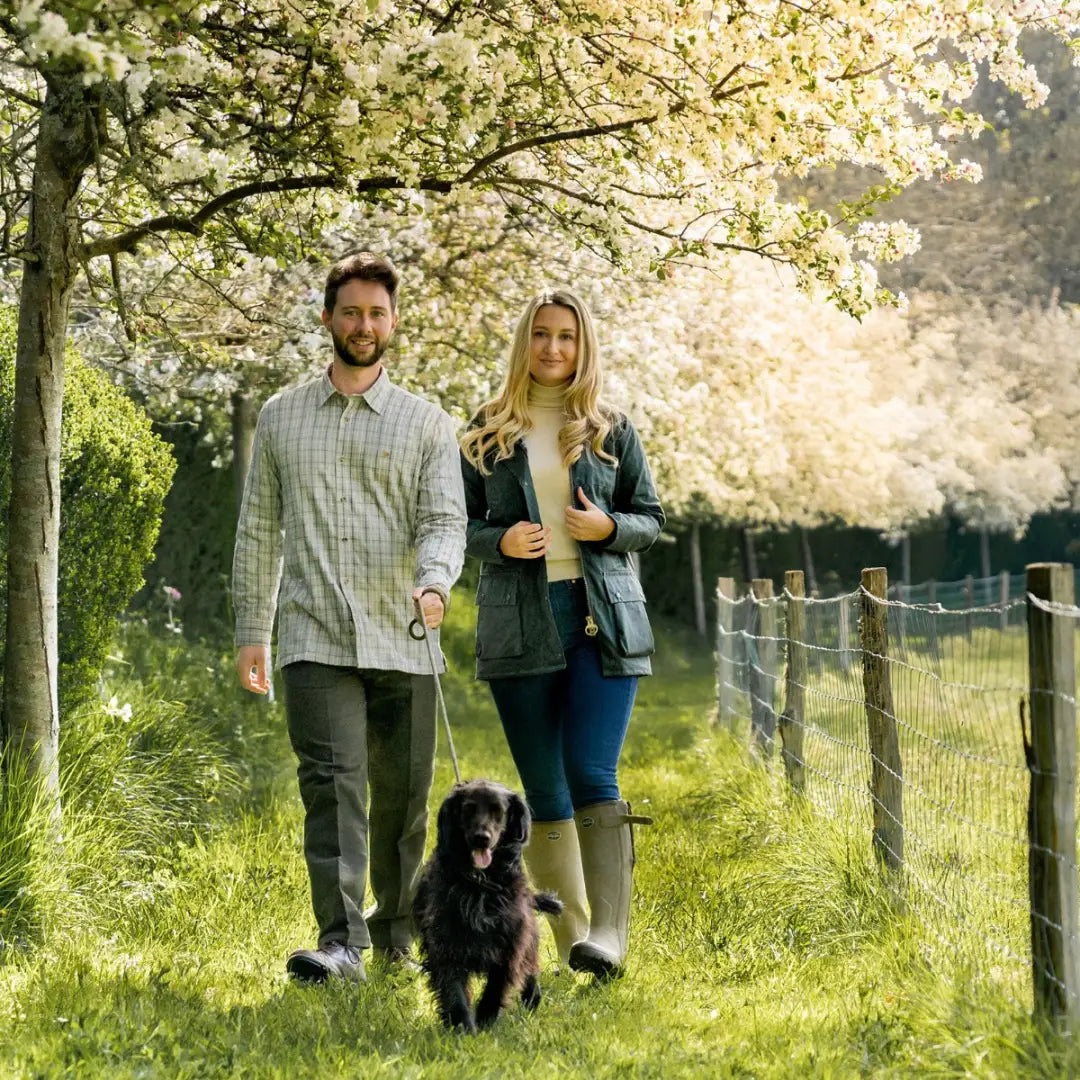 Couple in a fleece lined shirt walking a black dog under cherry blossoms