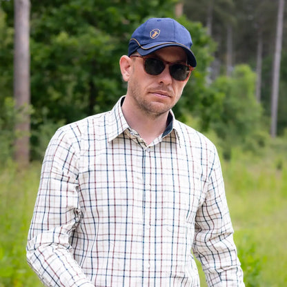 Man in plaid shirt, blue cap, and sunglasses rocking the Forest Skeet Cap outdoors