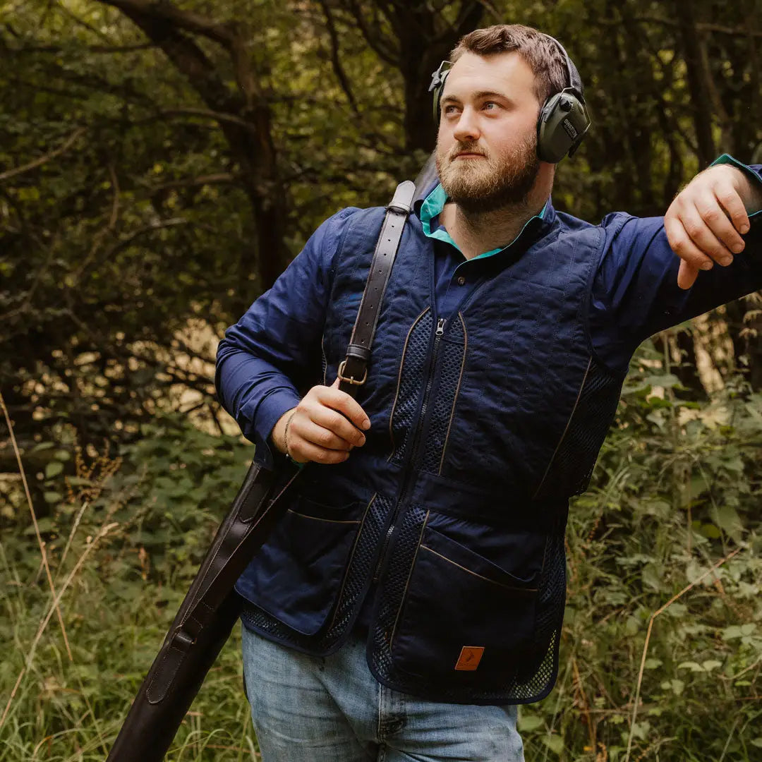 Man in navy jacket and headphones showing off the New Forest Skeet Vest in woods