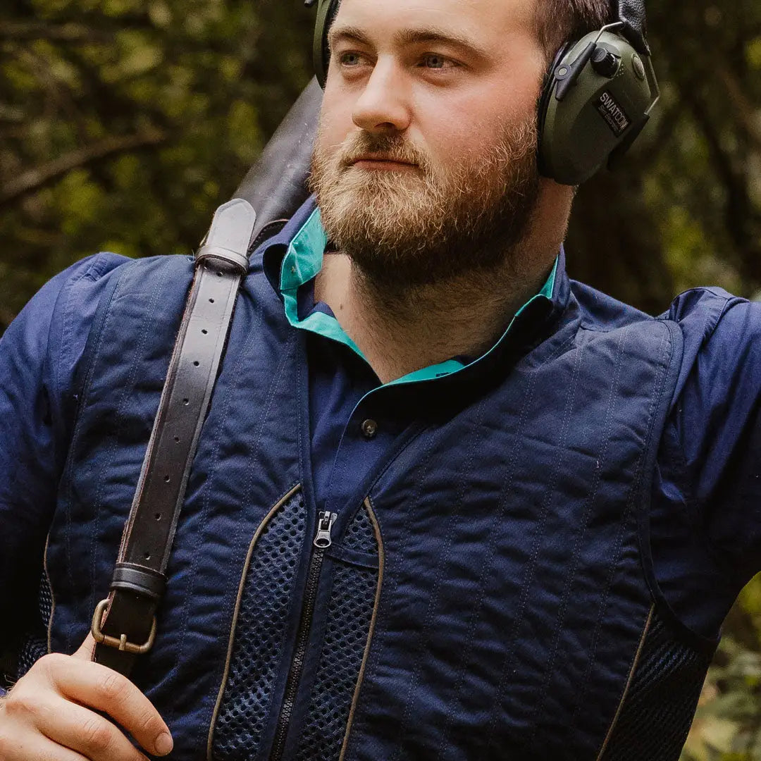 Bearded man in a navy blue Forest Skeet Vest with noise-cancelling headphones