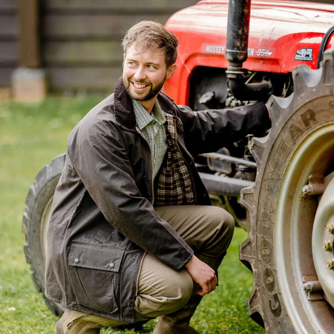 Red tractor with someone crouched by the wheel, perfect for outdoor vibes in a wax jacket