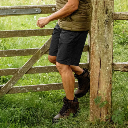 Person in a green vest and black forest trail shorts by a wooden fence outdoors