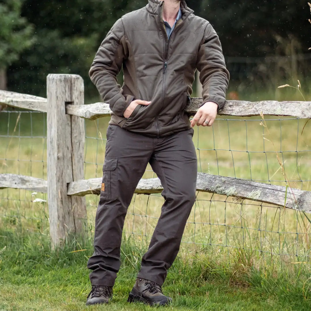 Man in a brown jacket and dark pants beside a wooden fence in Forest Trail Trousers