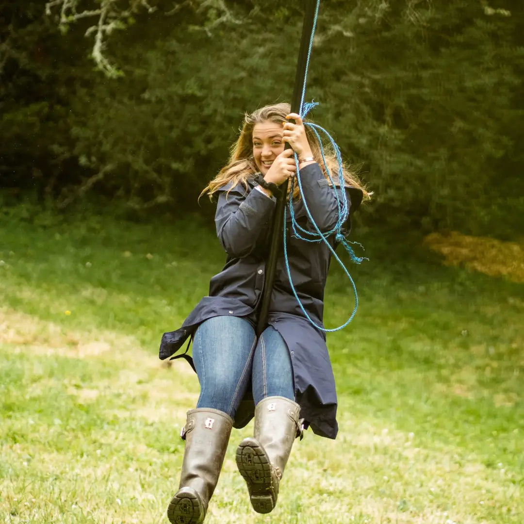 Person enjoying a rope swing wearing the New Forest Victoria length waterproof coat