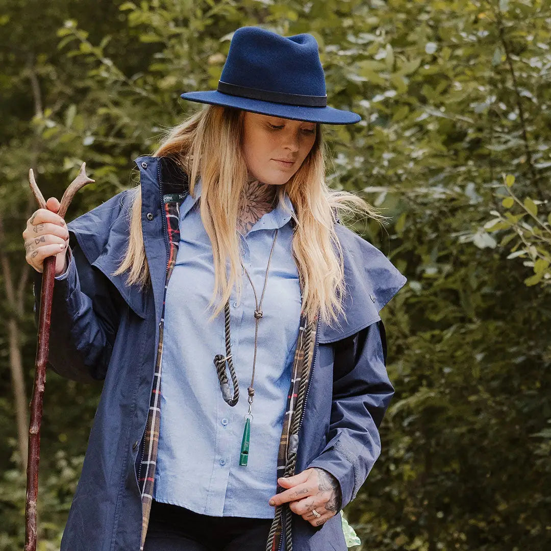 Woman in a blue hat and coat showcasing the New Forest Victoria Ladies Waterproof Coat outdoors