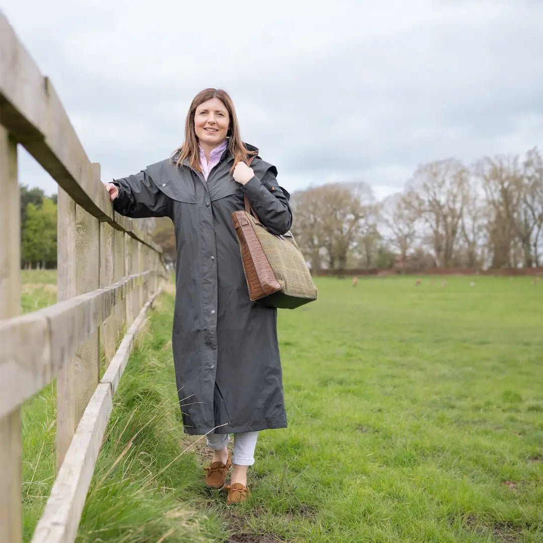 Woman in long gray Victoria Cape by a wooden fence, perfect for ultimate wet weather