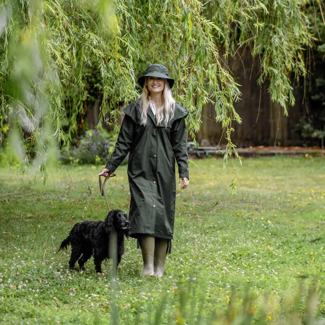 Woman in New Forest Victoria Cape walking black dog under willow tree in wet weather