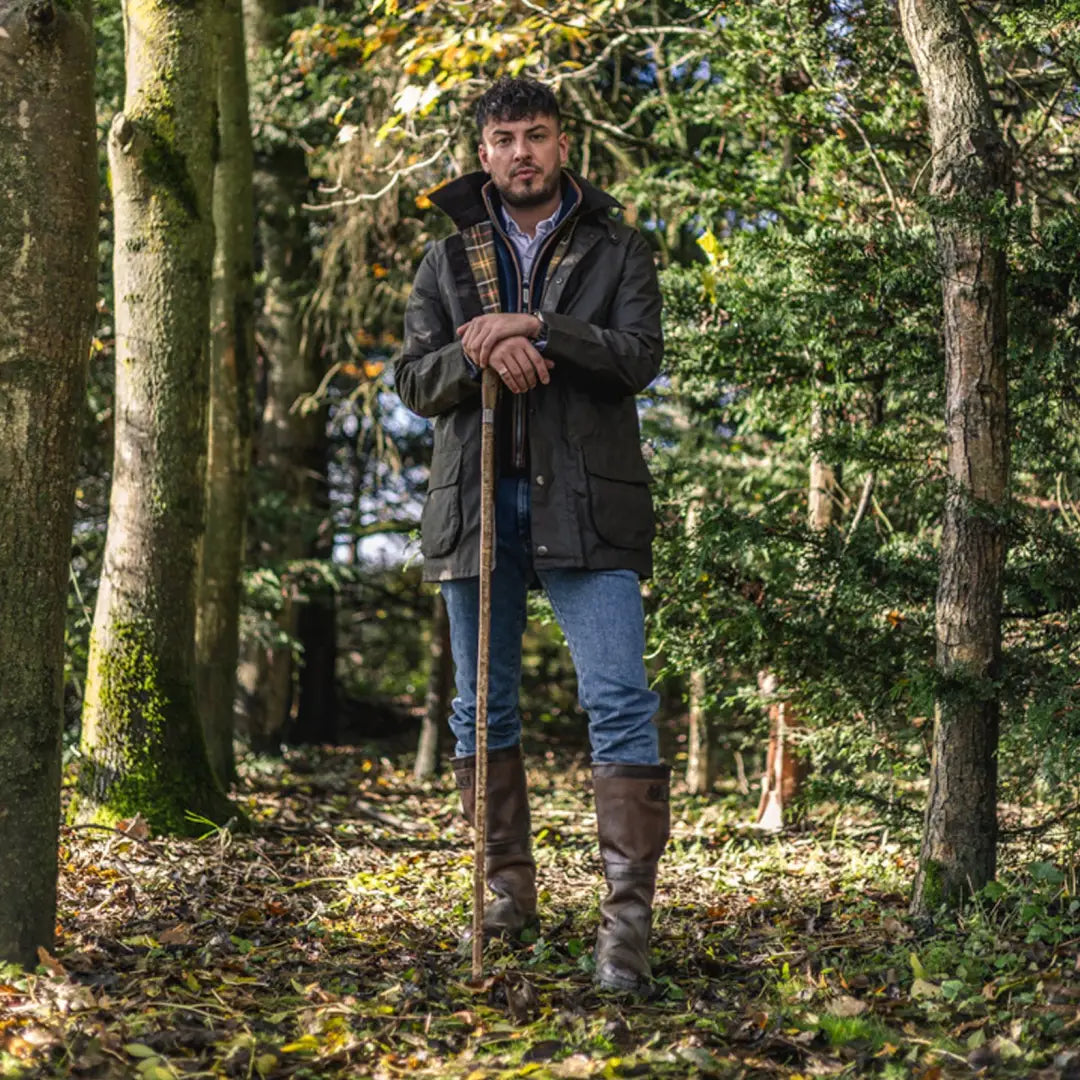 Man in a forest wearing a Woodsman Wax Jacket and boots, holding a walking stick