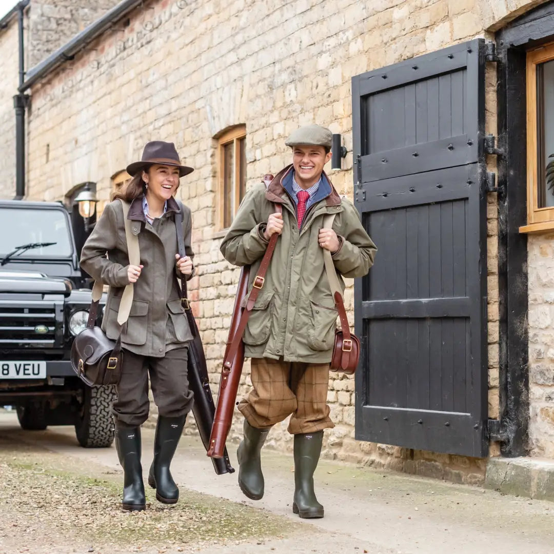 Two people in country attire with hunting gear, showcasing a leather shotgun slip