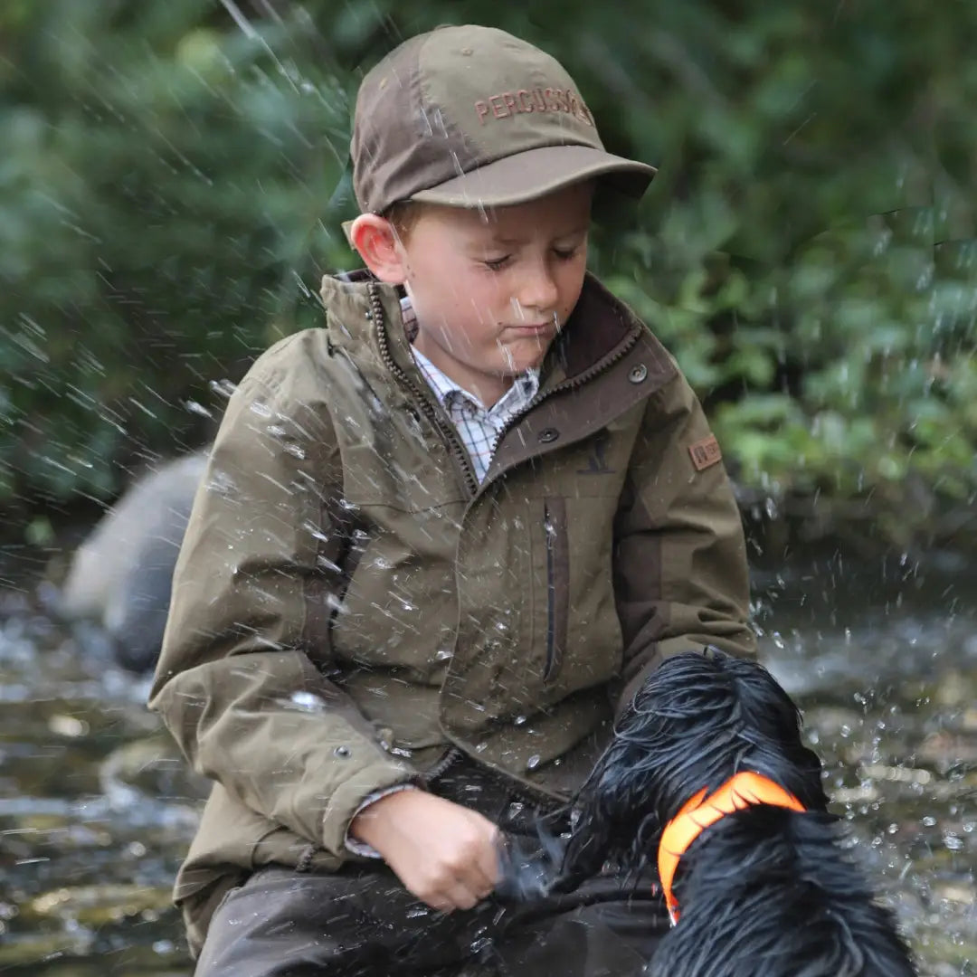 Young boy in Percussion Imperlight Kids jacket holds wet black dog in stream