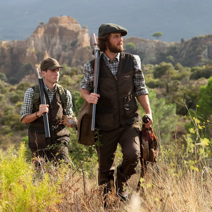 Two hunters in Percussion Tradition Trousers with rifles and a hunting dog in tall grass