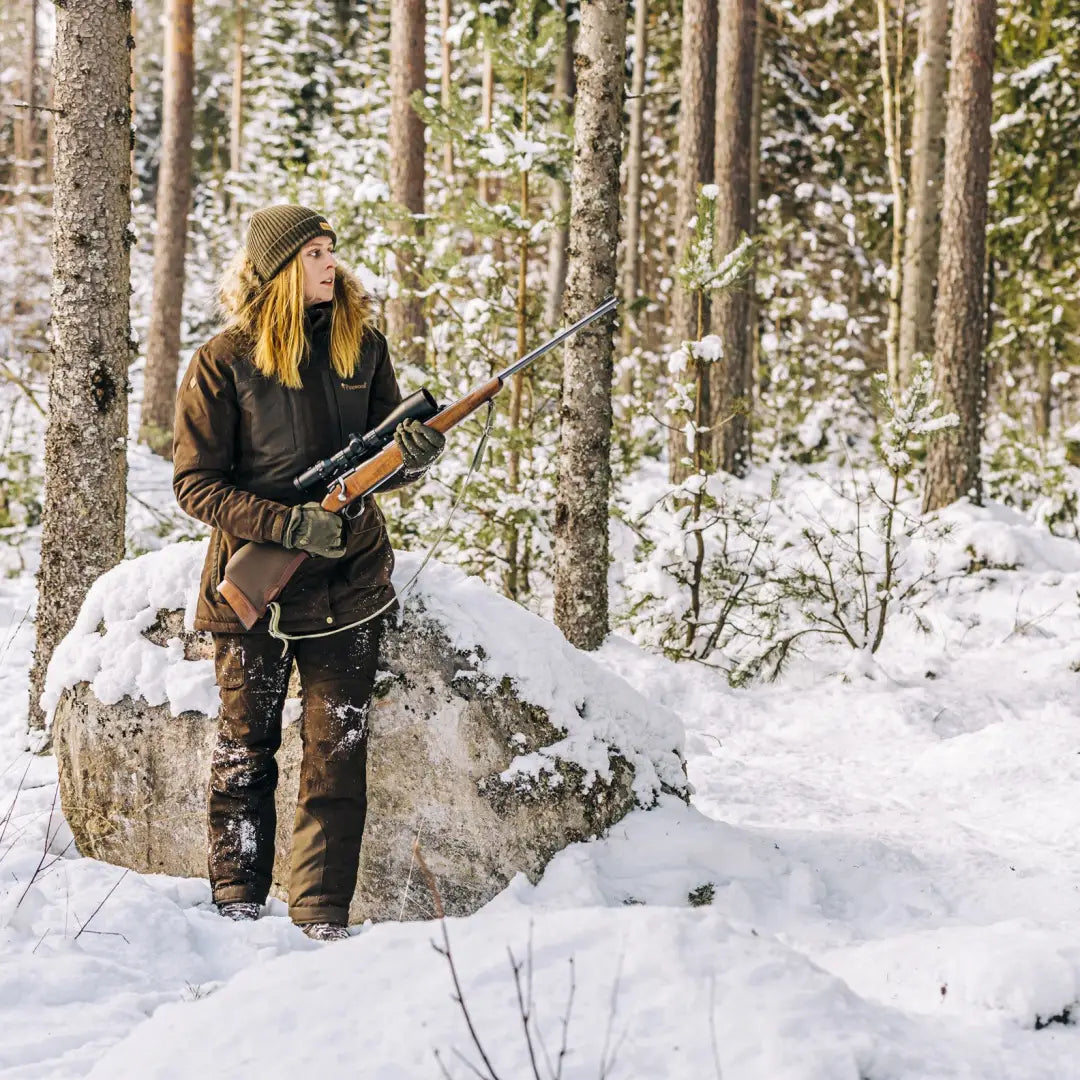 Woman in snowy forest wearing Pinewood Abisko 2.0 Ladies Hunting Jacket with rifle