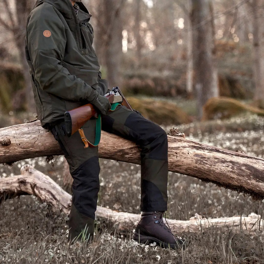 Person in Pinewood Caribou TC Extreme Trousers enjoying hiking adventures on a fallen tree