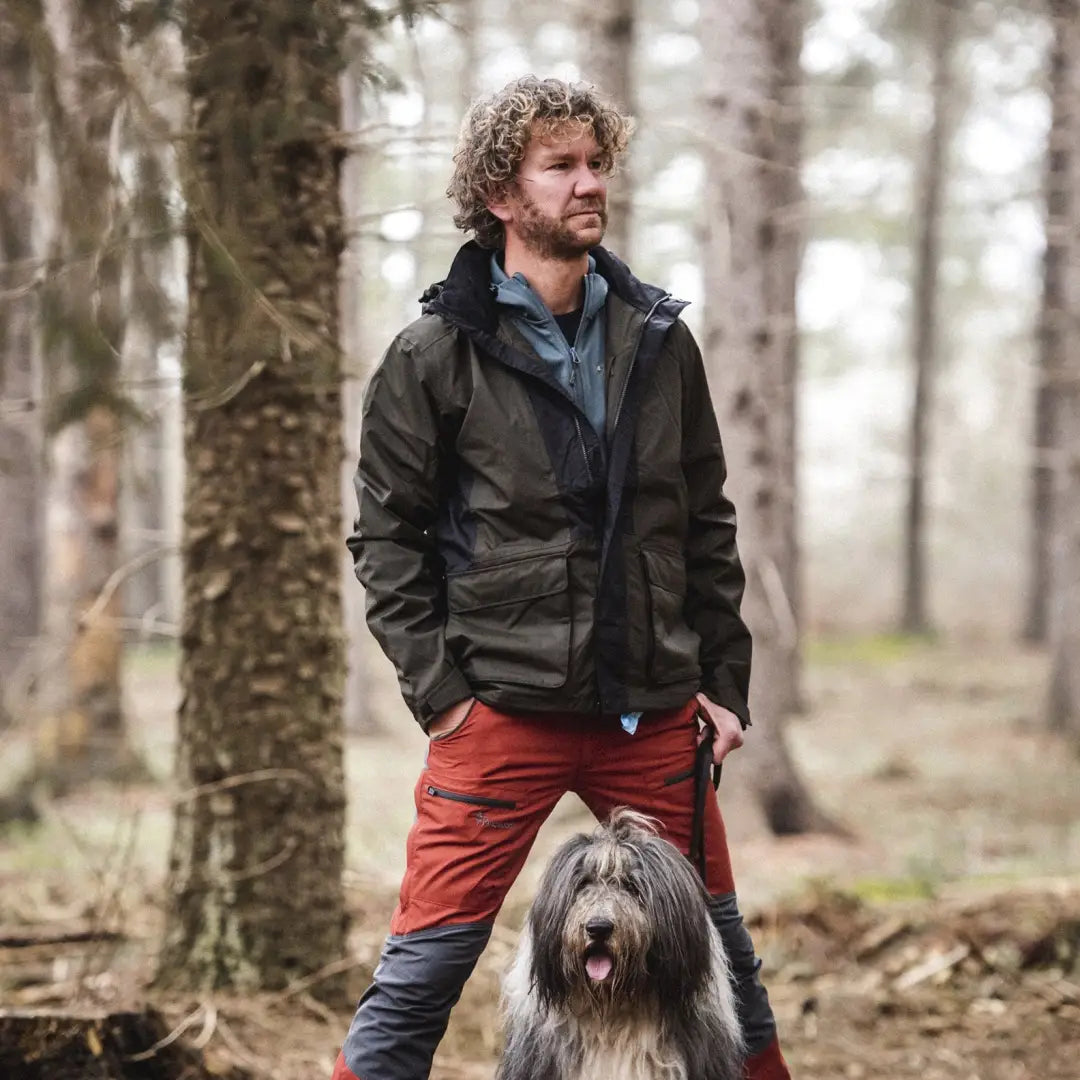 Man with curly hair in a dark jacket and red pants with shaggy dog in Pinewood forest