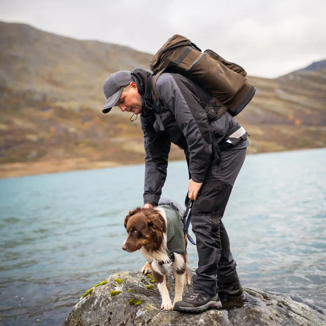 Hiker in a Pinewood Finnveden Hybrid Extreme Jacket pets a dog by the water