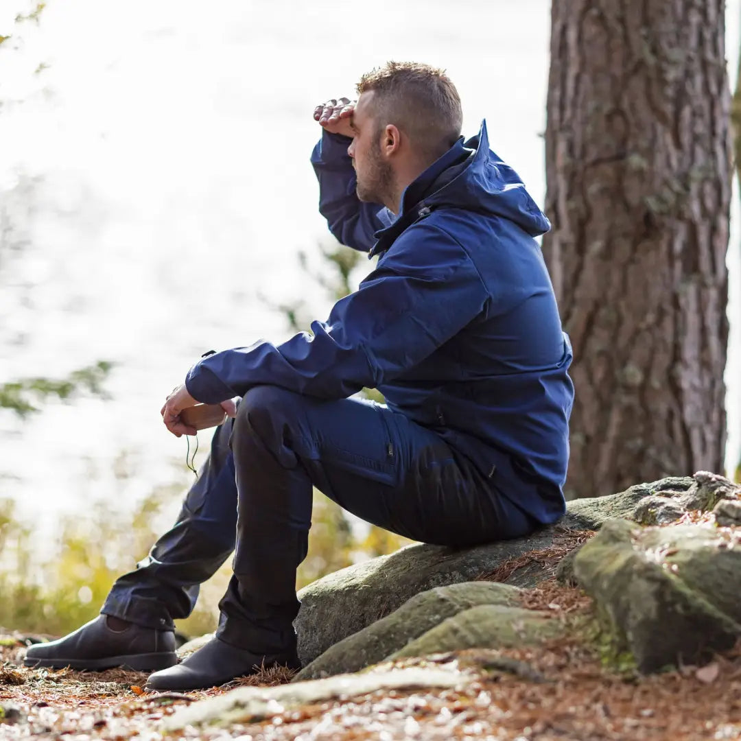 Man in a blue jacket on a rock showcasing Pinewood Finnveden Hybrid Men’s Jacket