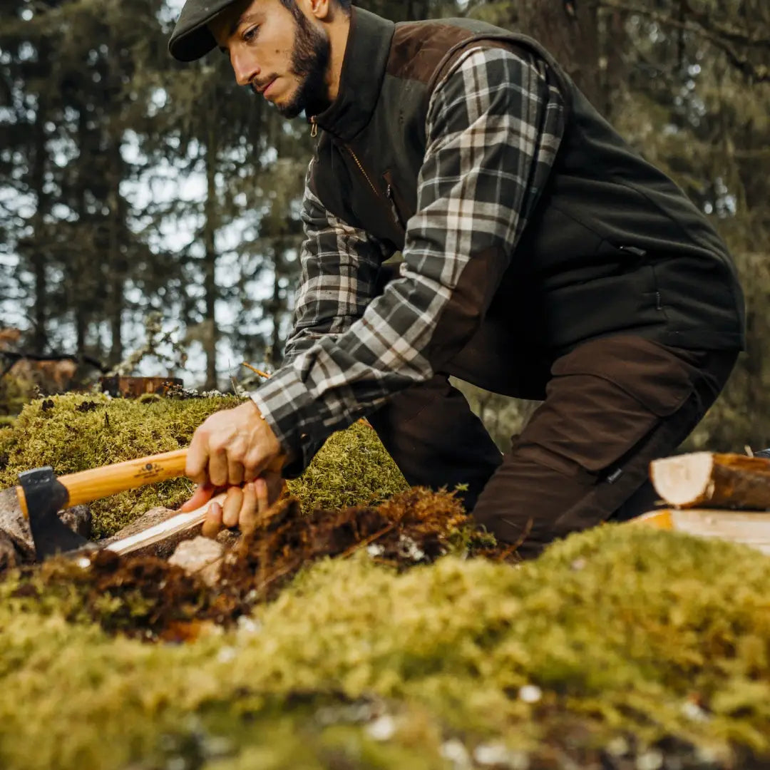 Man wearing plaid shirt and vest using tool on mossy ground in Smaland Light Trousers