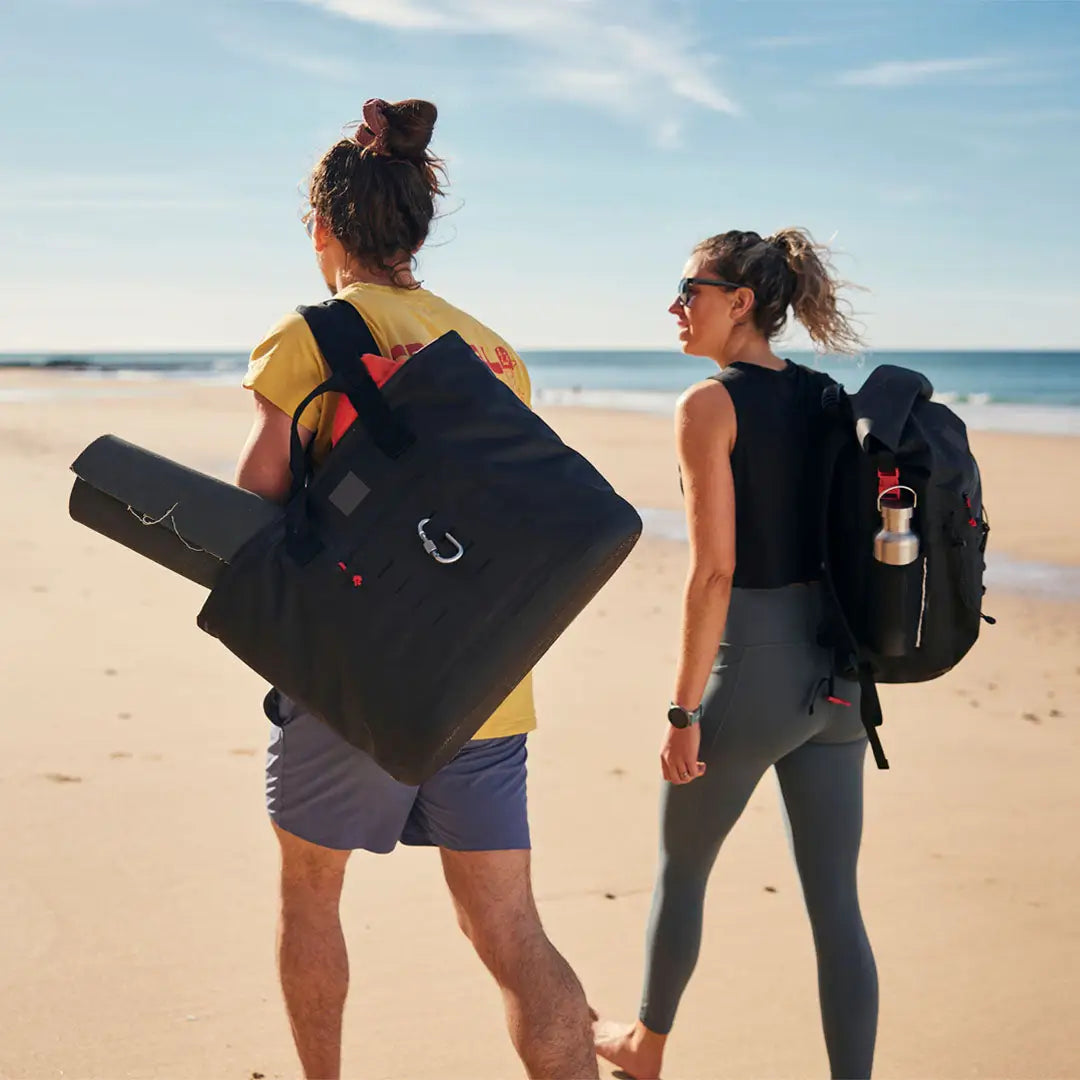 Two people walking on the beach with a red waterproof tote bag in hand