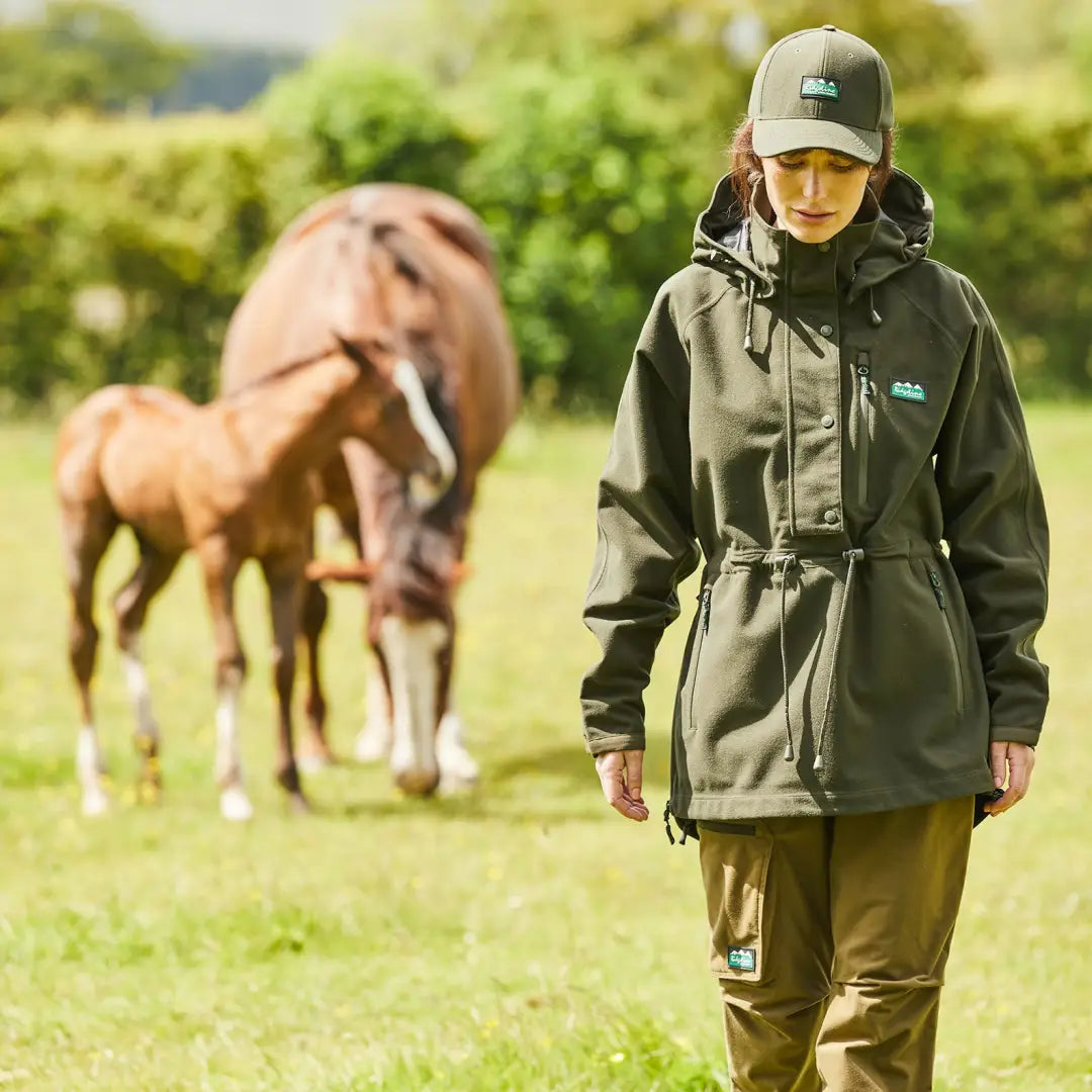 Person in green Ridgeline Ladies Monsoon II Smock walking near horses in the countryside