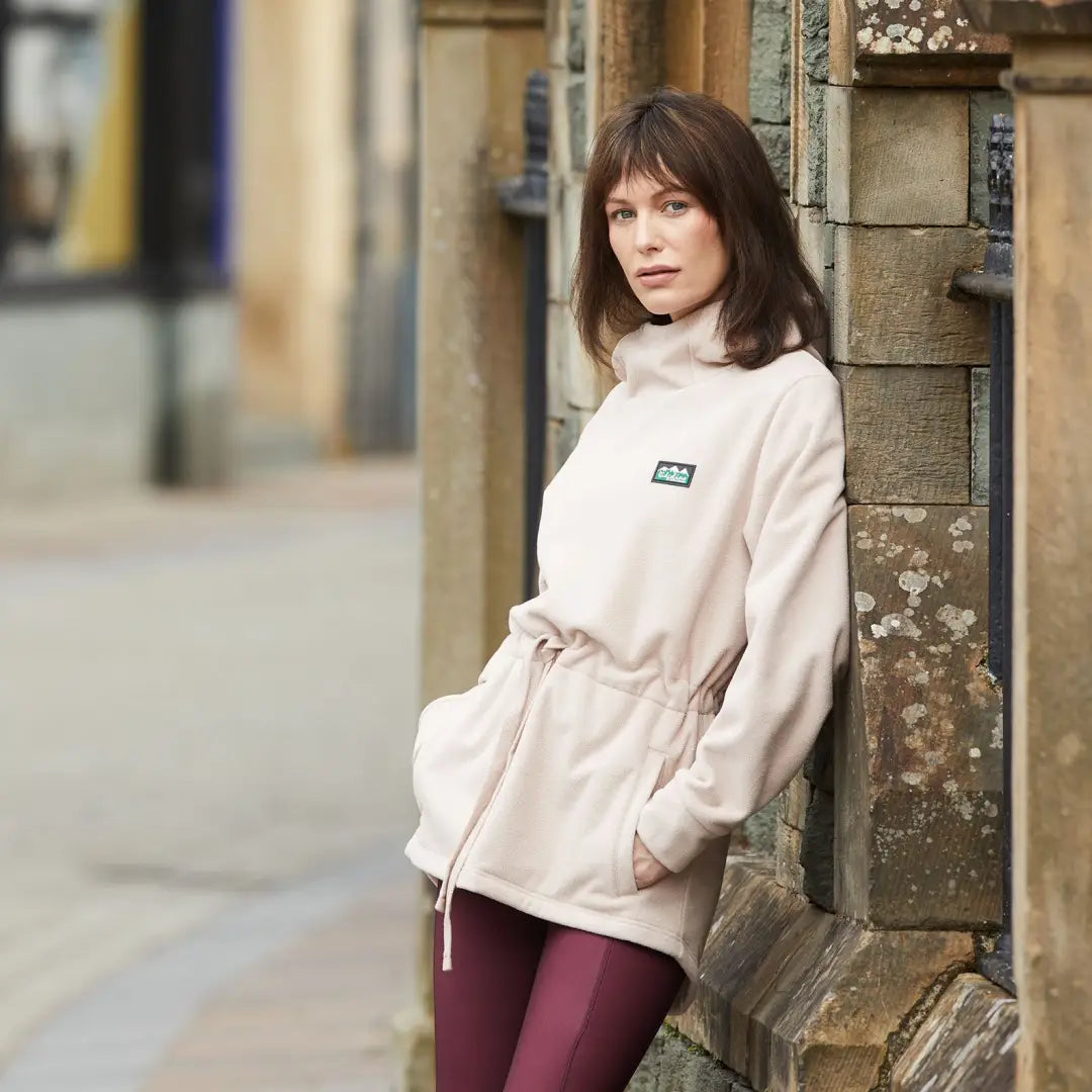 Woman in cream jacket by a stone wall, showcasing Ridgeline Salt Marsh Fleece