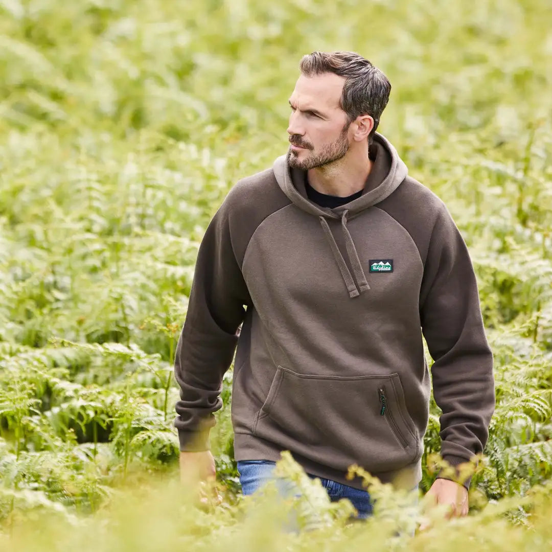 Man in a brown North Island Hoodie standing amidst lush vegetation