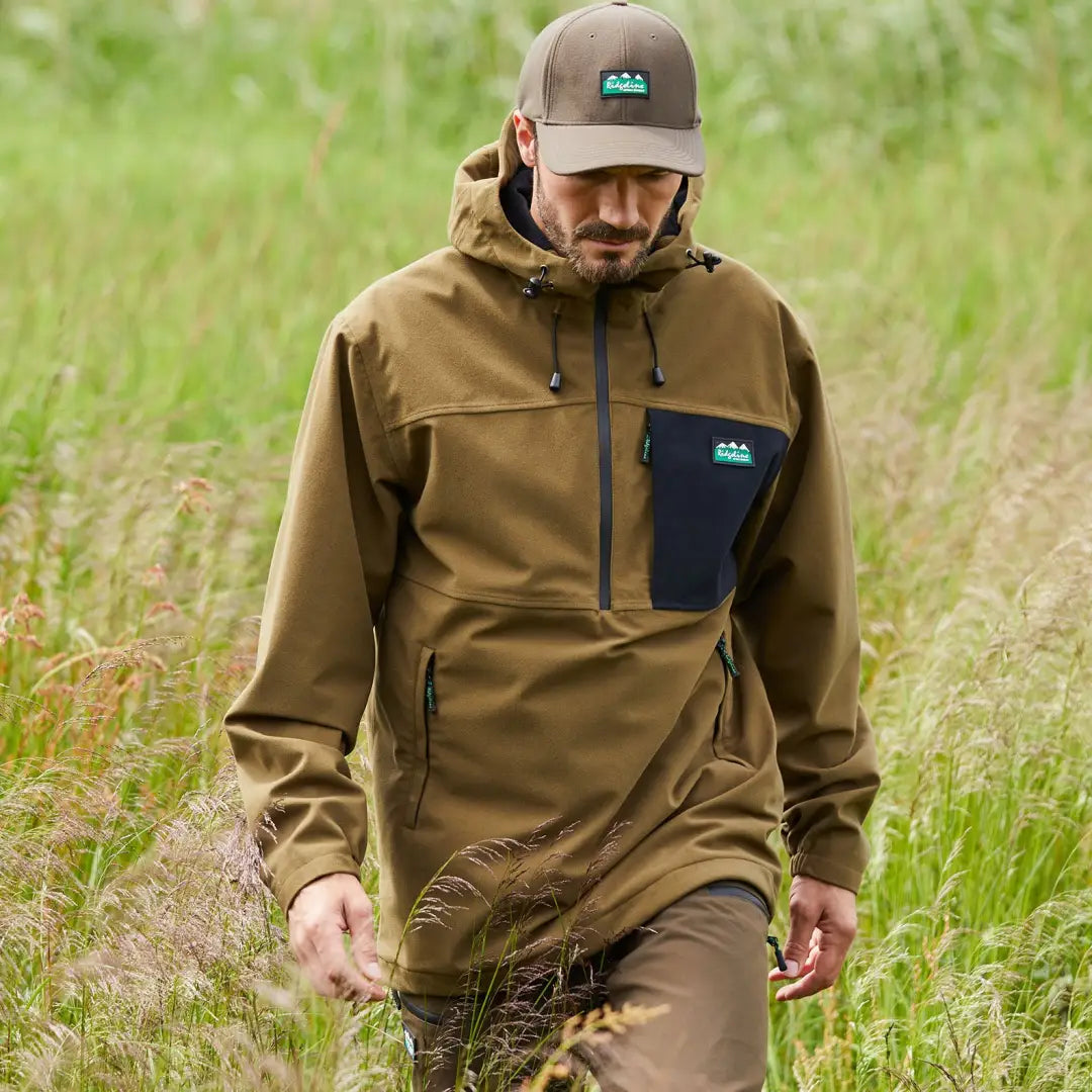 Bearded man in a brown hooded jacket walks through grass wearing Ridgeline Tempest Smock