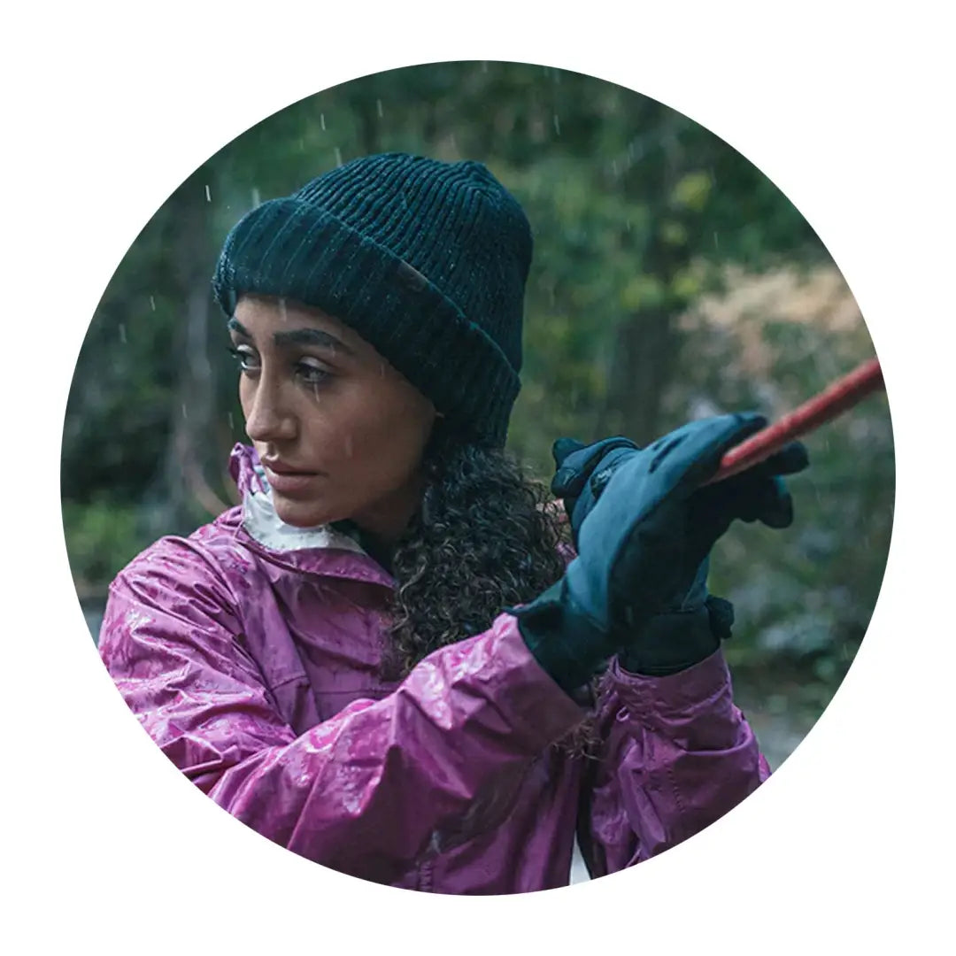 Woman in a pink raincoat and dark knit hat with her red tool, showcasing the Bacton Hat