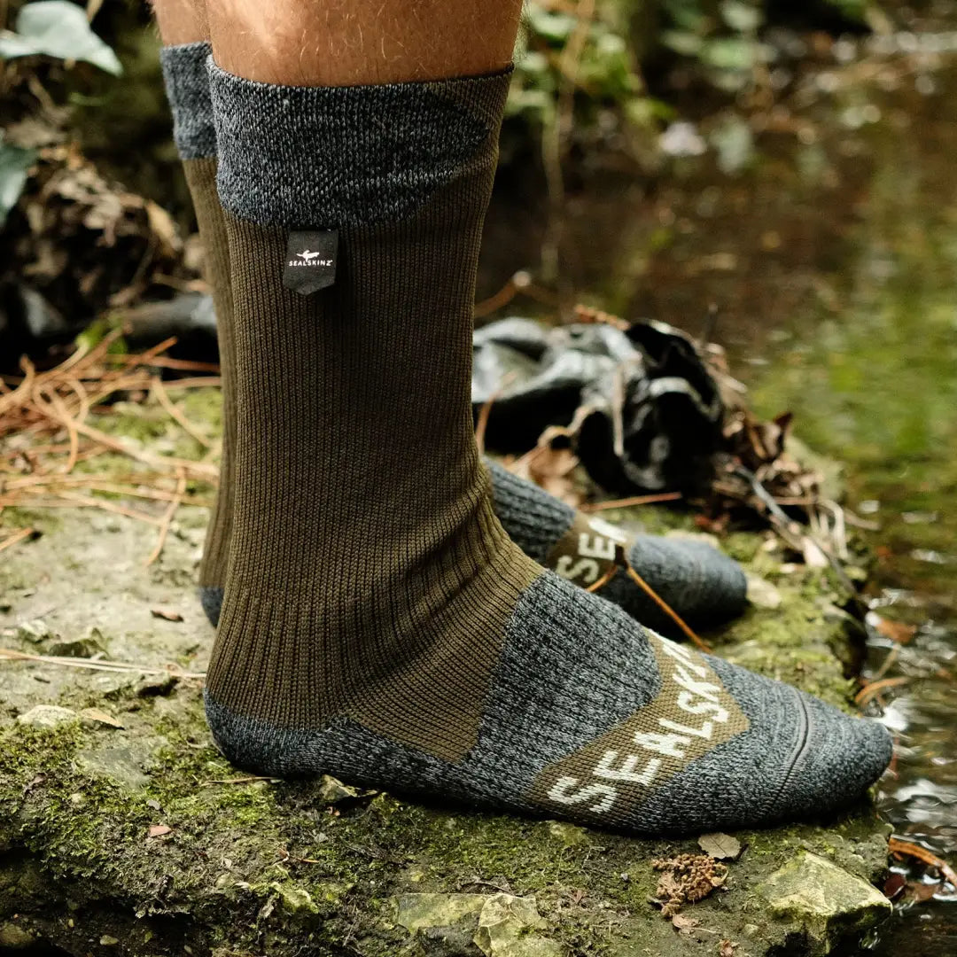 Olive green and gray Sealskinz Raynham Waterproof Sock worn with sandals on rocky ground