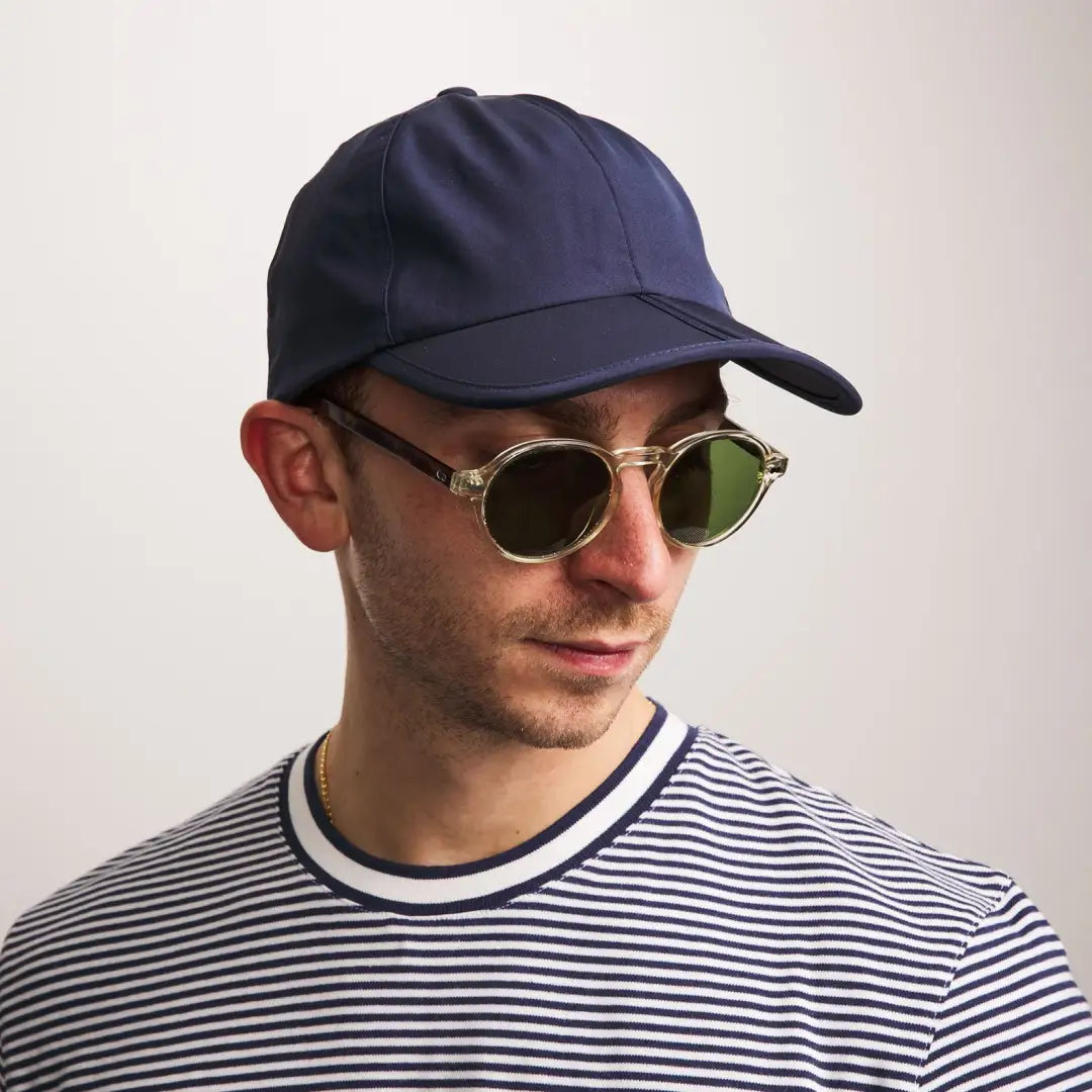 Person in a navy Sealskinz Salle Cap, round shades, and a stylish striped shirt