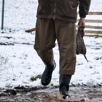 Person in Buckthorn Short Overtrousers holds a dead bird in snowy, muddy terrain