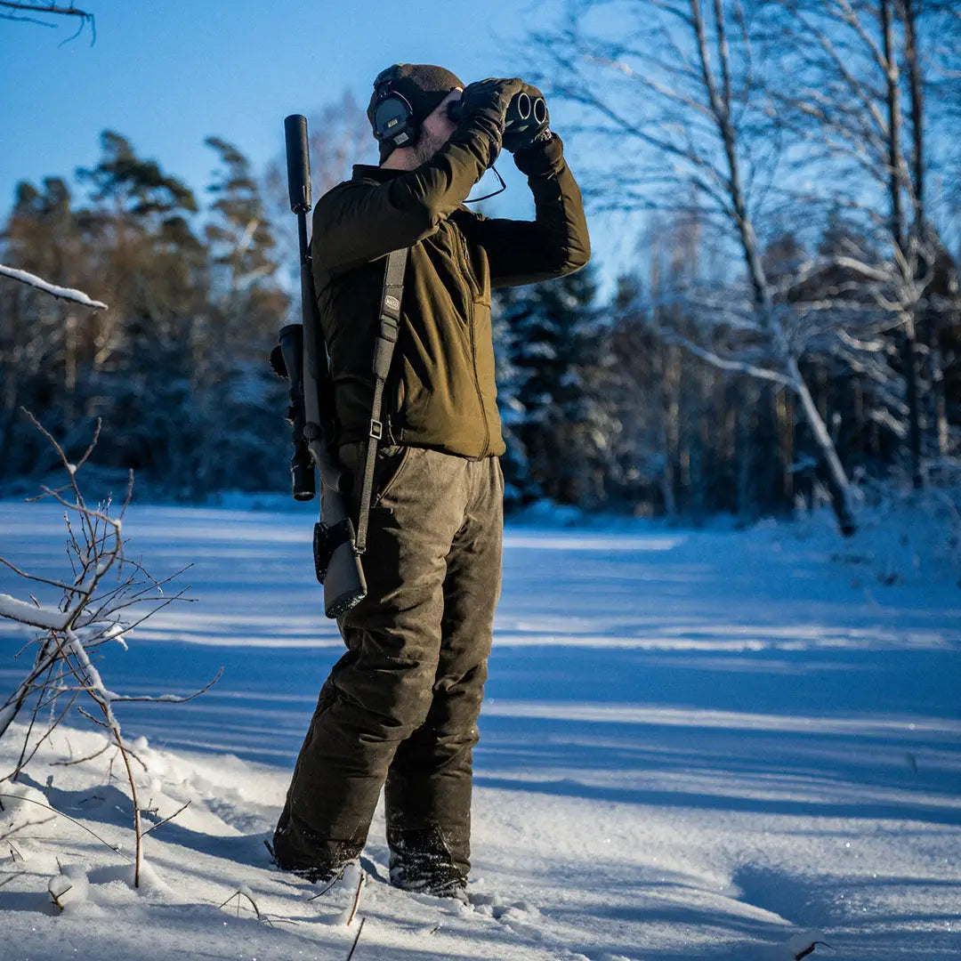 Person in winter gear using binoculars in snow while wearing Seeland Celsius Heat Jacket