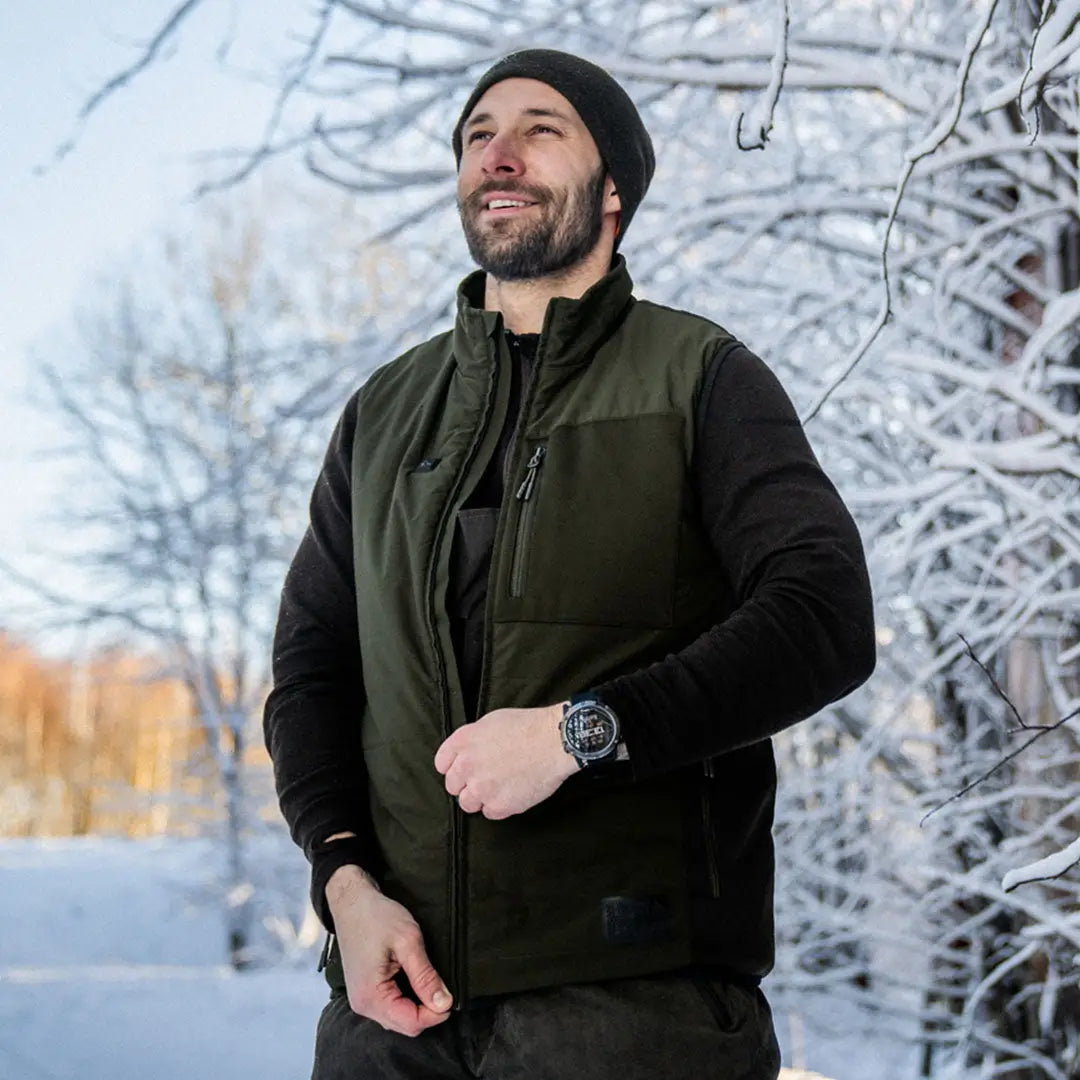 Man in green Celsius Heat Waistcoat and black beanie enjoying the snowy outdoors