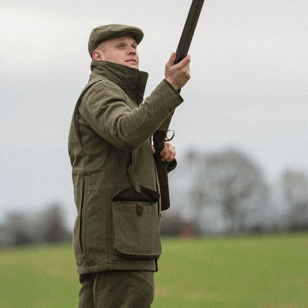 Hunter with a shotgun in a field wearing a Seeland Hillside Jacket