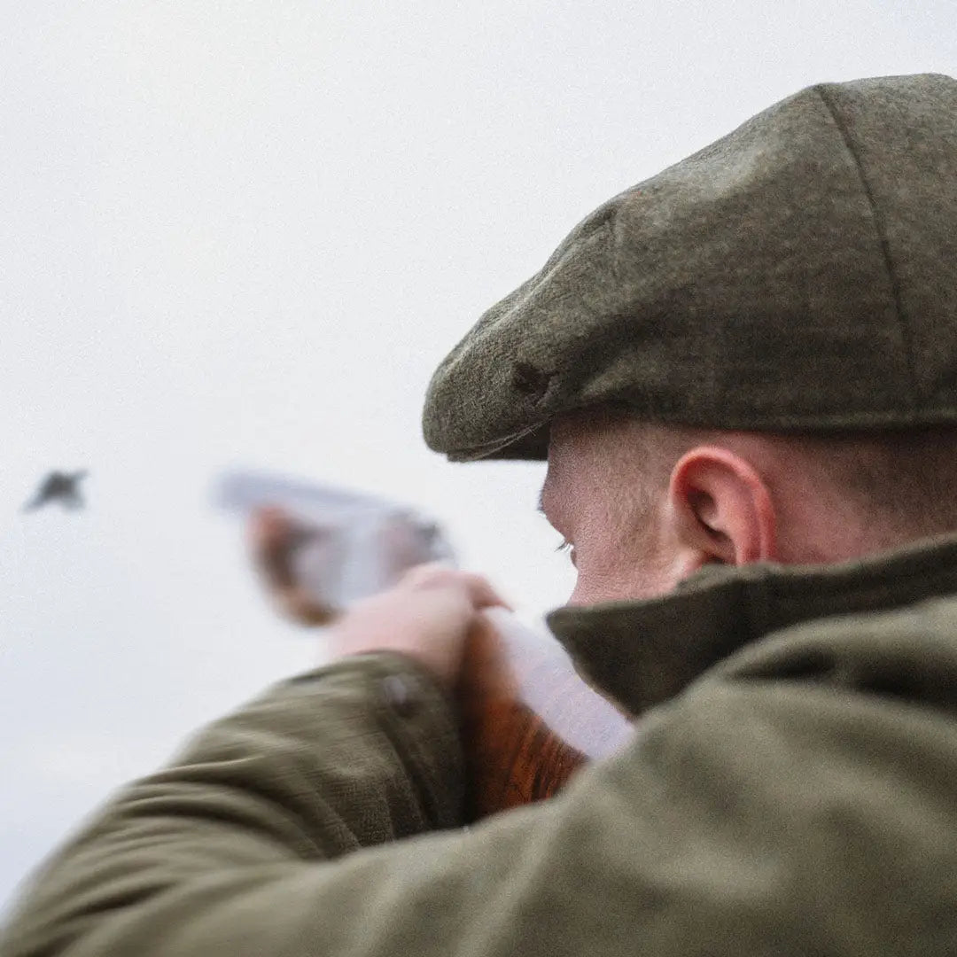 Flat cap on a hunter aiming a shotgun, perfect for country clothing and outdoor adventures