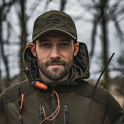 Bearded man in a green cap and dark jacket showcasing the Seeland Trax Cap