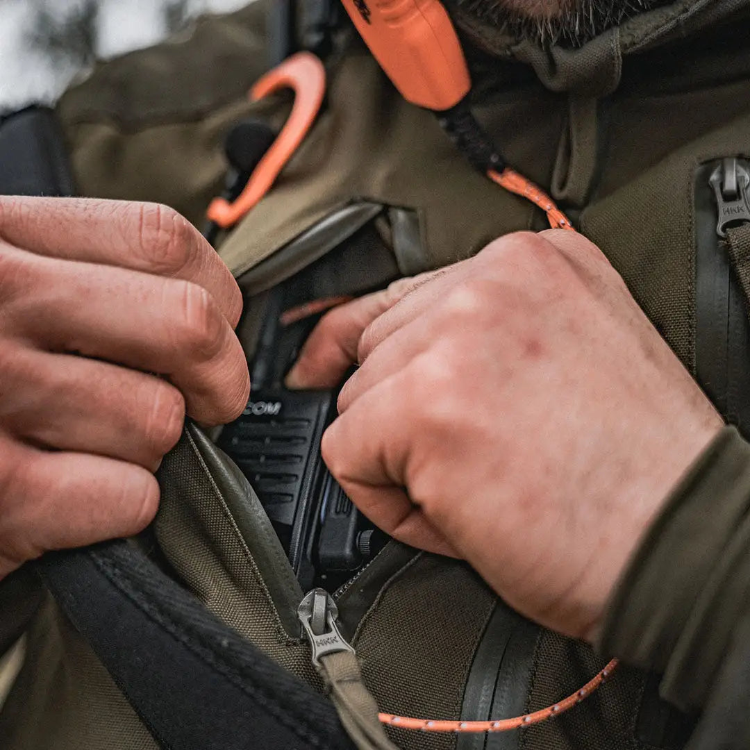 Hands fastening the zipper on a Seeland Trax Jacket in olive green