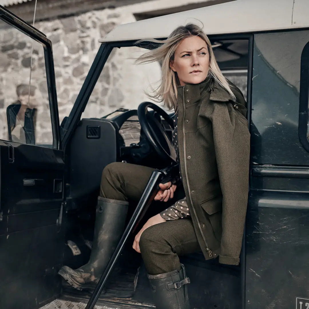 Woman in outdoor gear relaxing by her rugged ride in a Woodcock Advanced Jacket