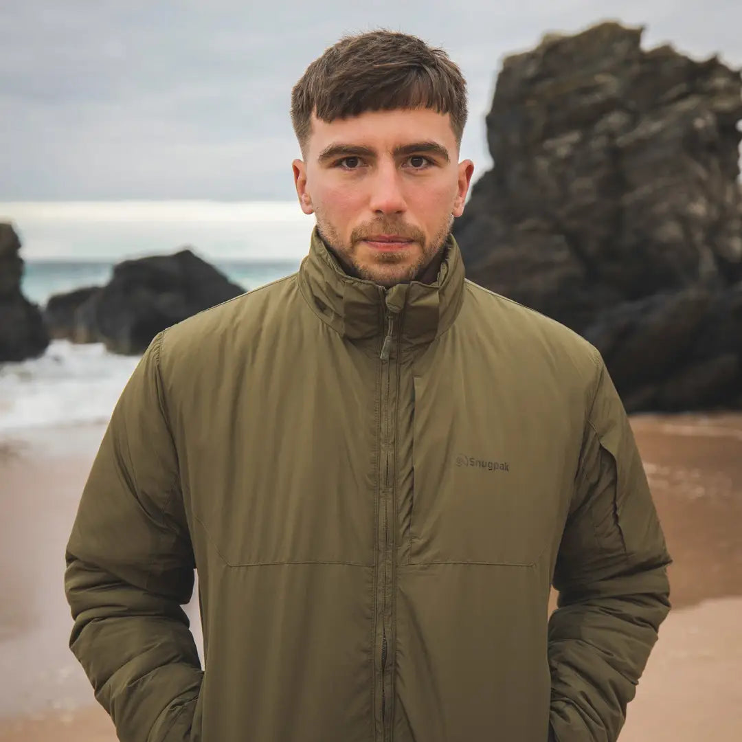 Man in olive green Snugpak Arrowhead Jacket on beach, a best selling Sleeka elite