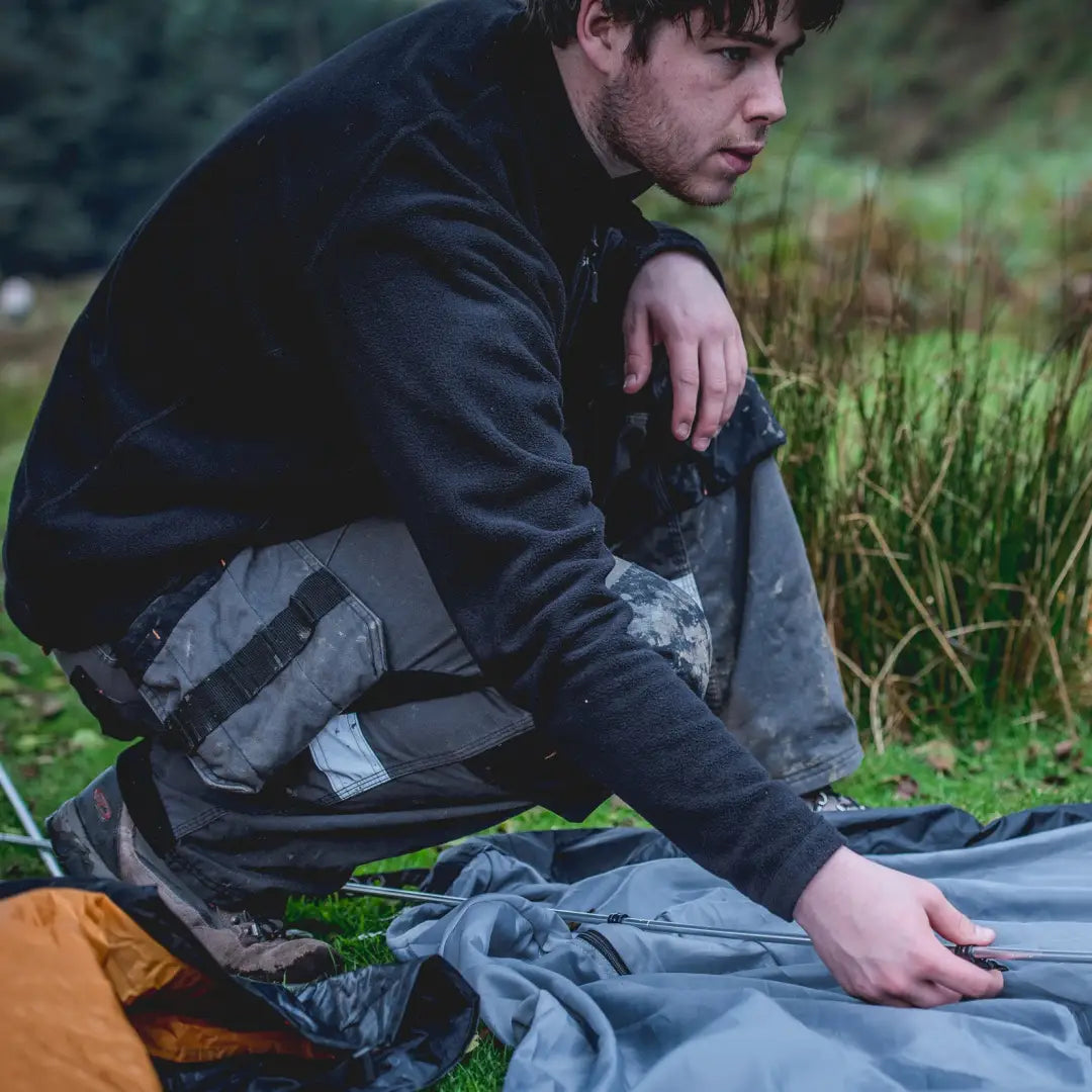 Man crouching outdoors with Snugpak Impact Fleece while managing camping gear