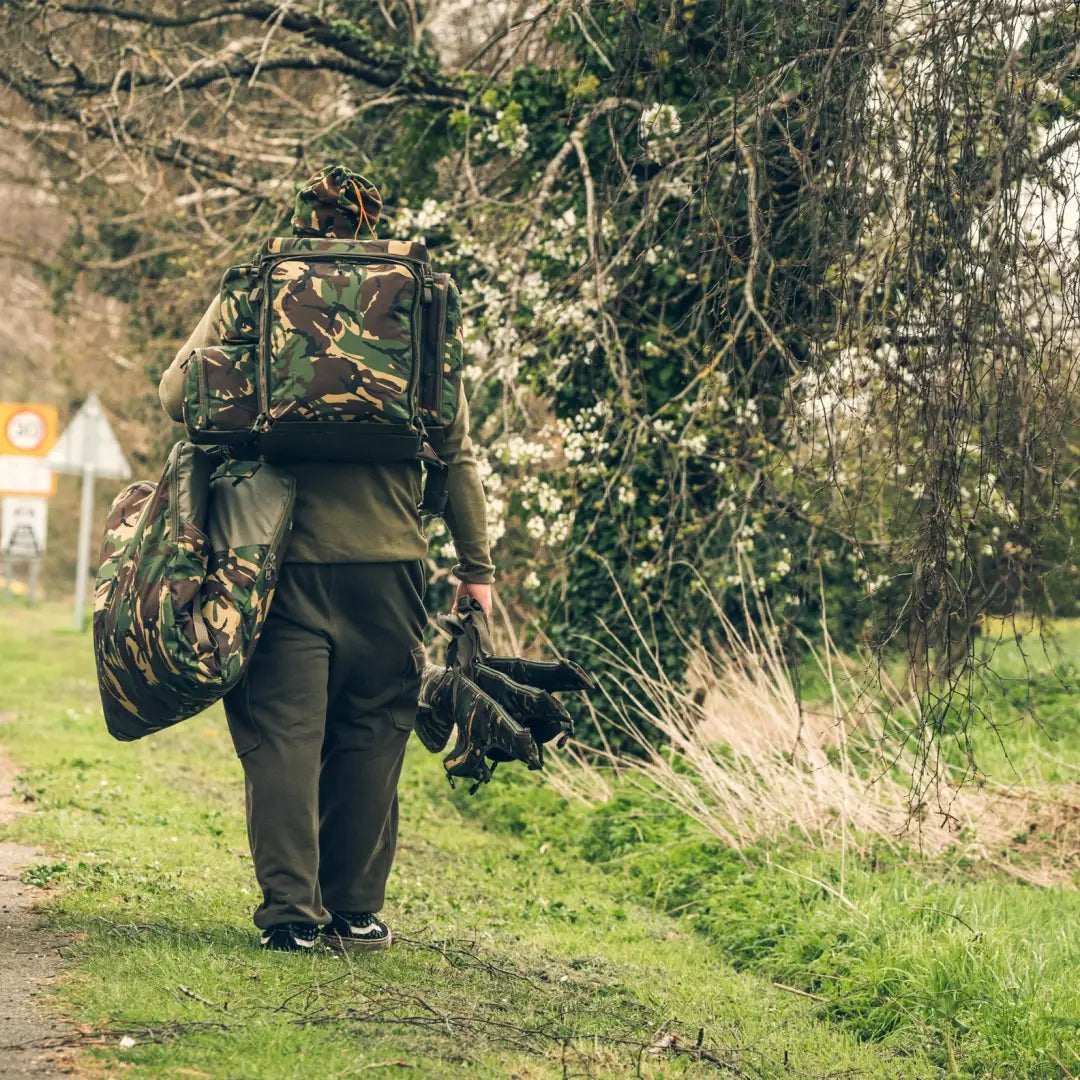 Camouflage-clad person with Speero Adjustable Rod Sleeve hiking on a scenic path